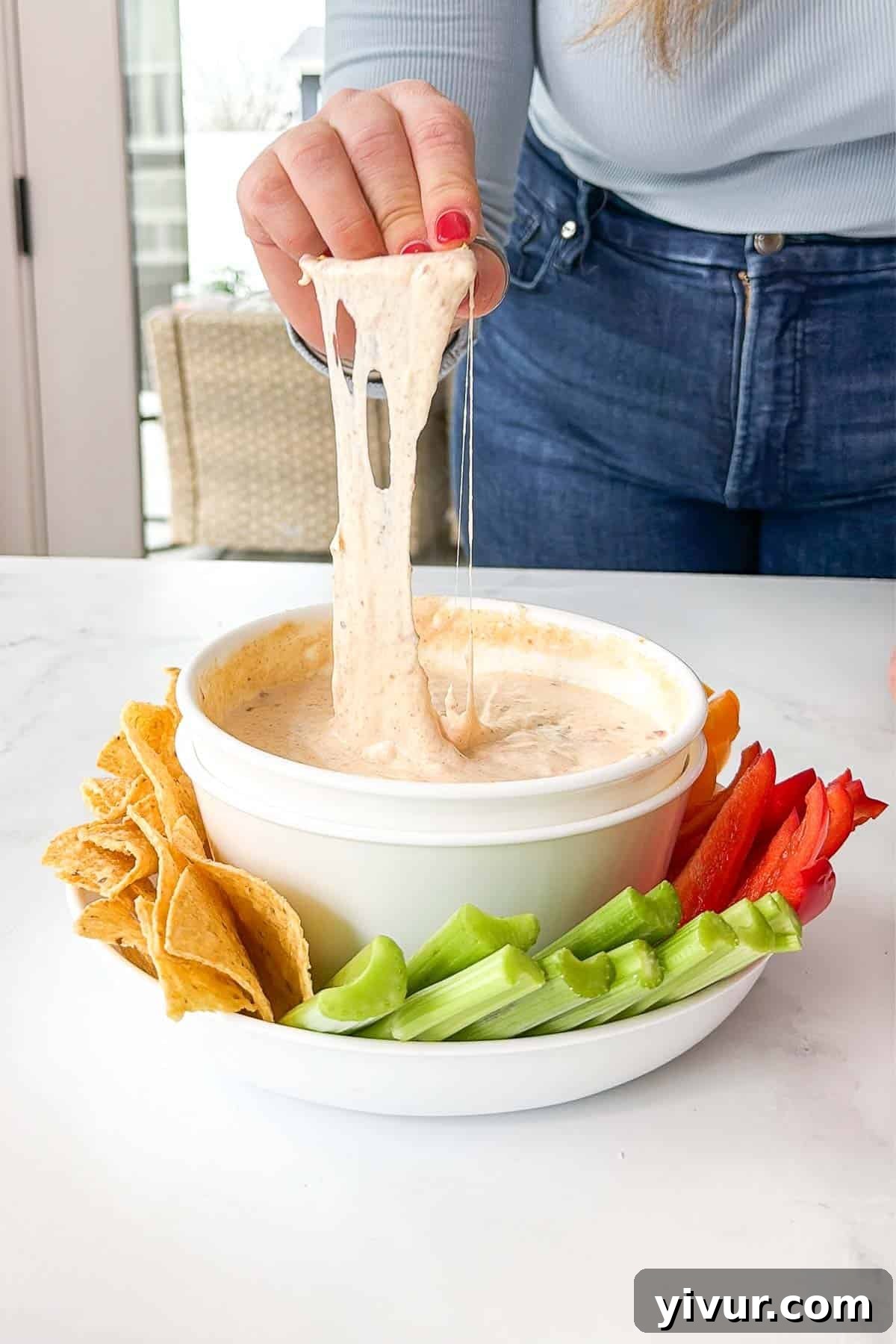 Protein-Boosted Cottage Cheese Queso 2 Creamy High Protein Queso Dip in a white bowl, garnished with cilantro, served with tortilla chips and fresh vegetables.