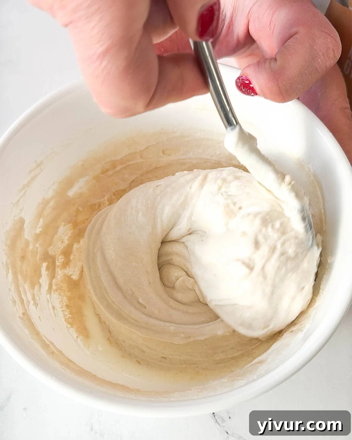 A close-up image showing a bowl where nonfat Greek yogurt and vanilla protein powder are being thoroughly mixed together with a spoon until smooth and well combined.