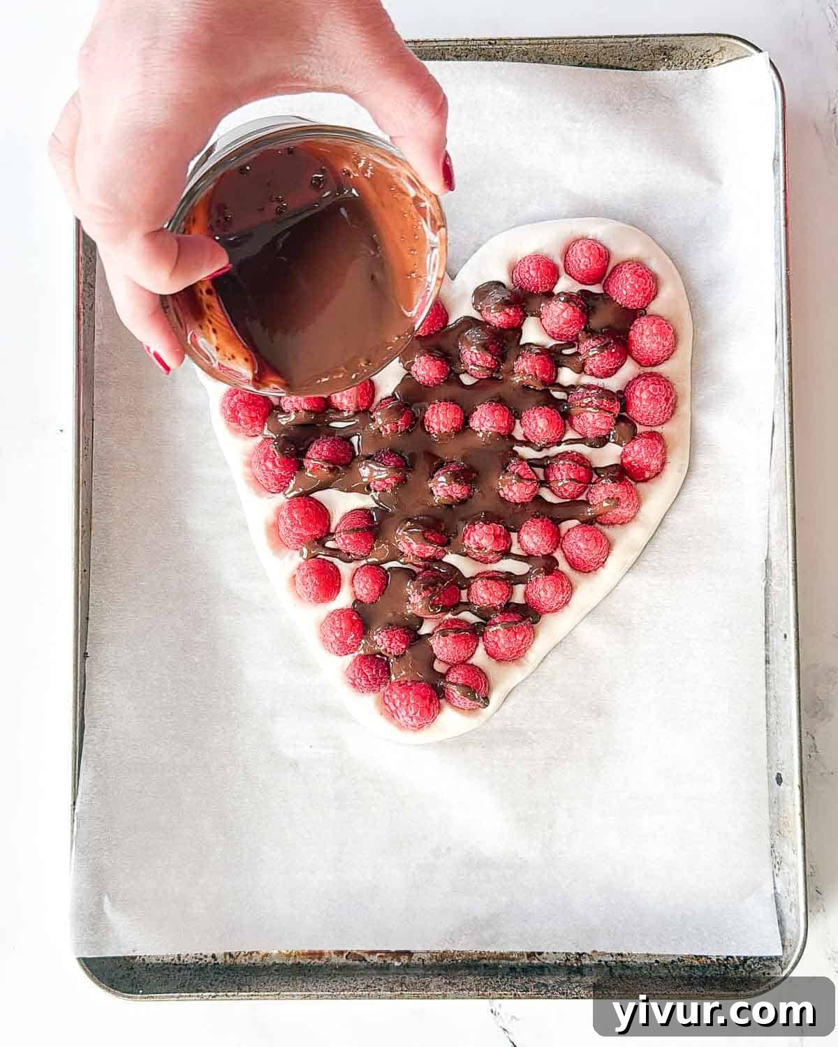 Melted dark chocolate, mixed with coconut oil, is being artfully drizzled in thin streams over the raspberry-studded Greek yogurt heart, ready for freezing.