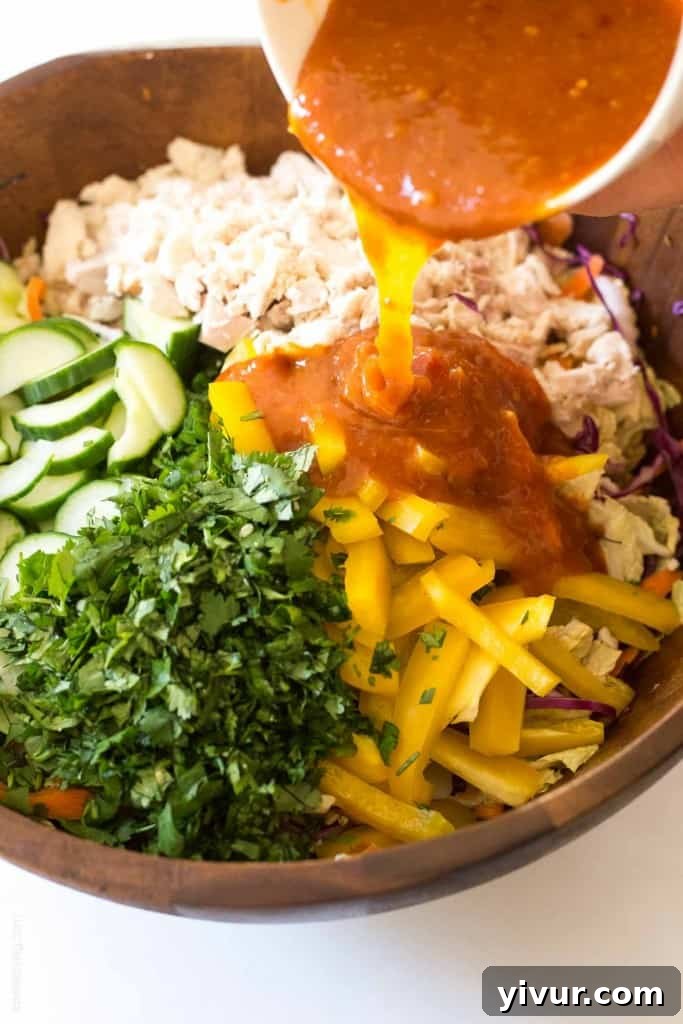 Hand tossing the colorful Rainbow Chopped Thai Chicken Salad with dressing