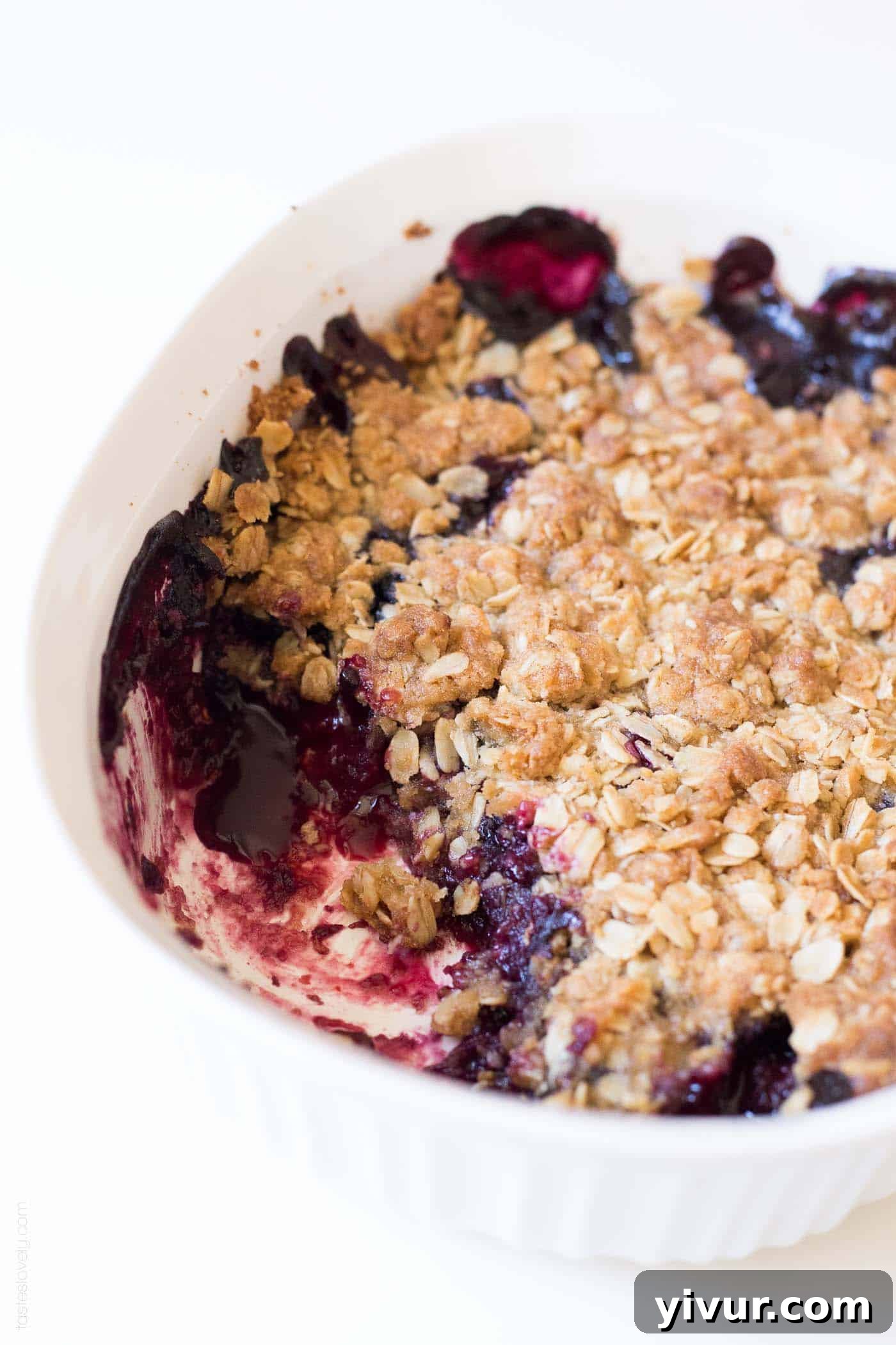 Quick Triple Berry Crumble from Frozen 6 A baked triple berry crumble with one scoop removed, showing the luscious fruit filling and crunchy oat topping.