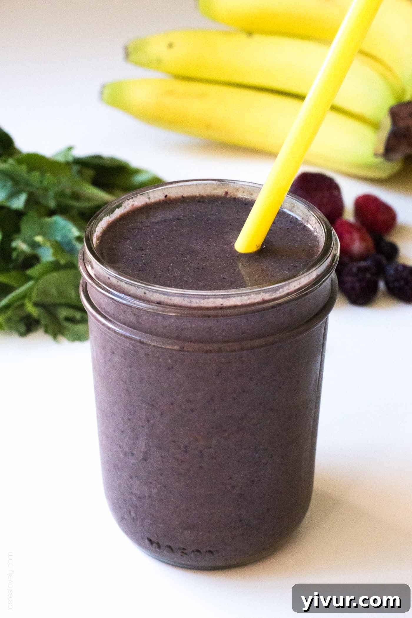 Close-up of a glass mason jar filled with a thick, vibrant superfoods pregnancy smoothie, topped with a yellow straw.