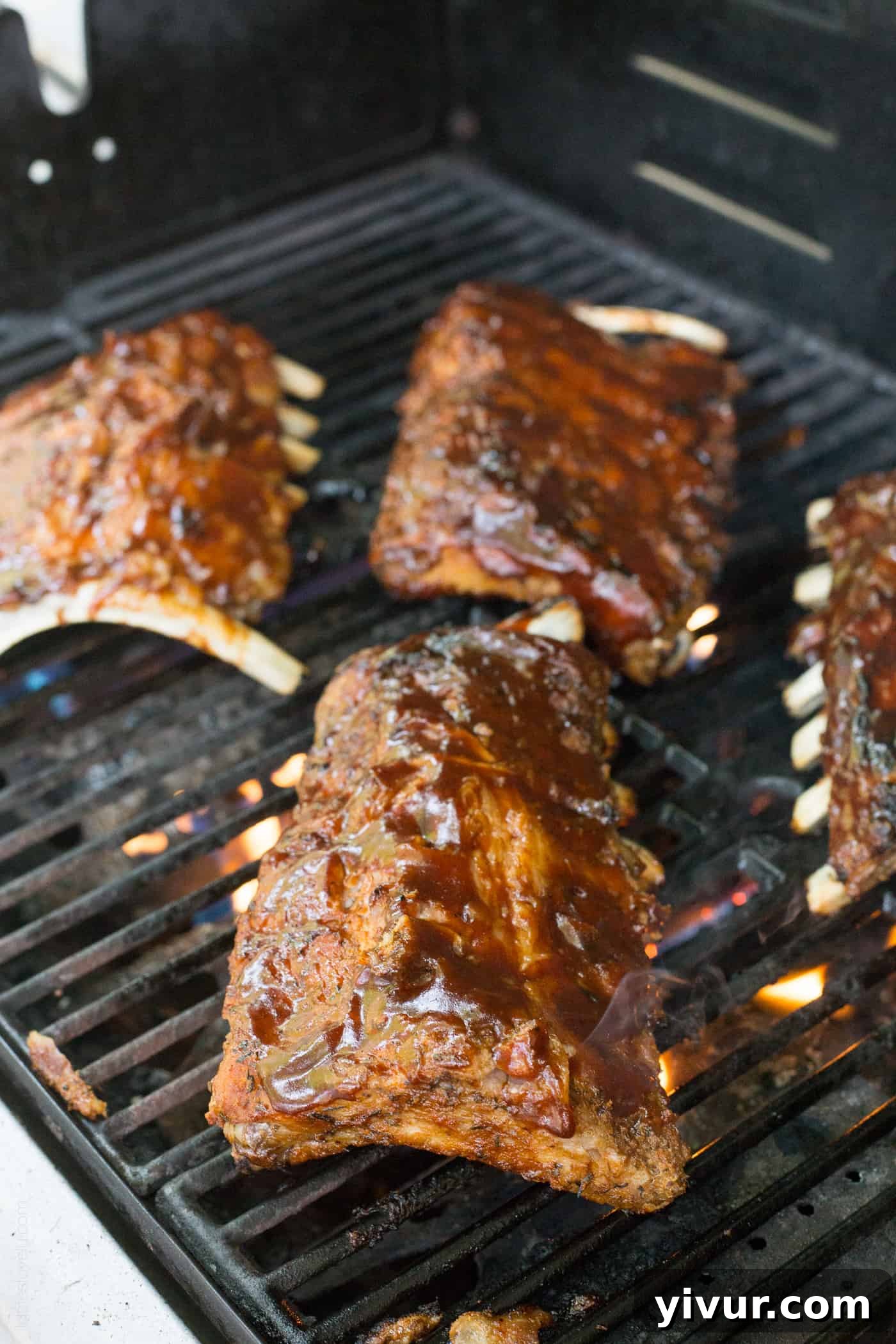 Several racks of Dr Pepper ribs with caramelized BBQ sauce cooking on a hot grill, showing distinct grill marks.
