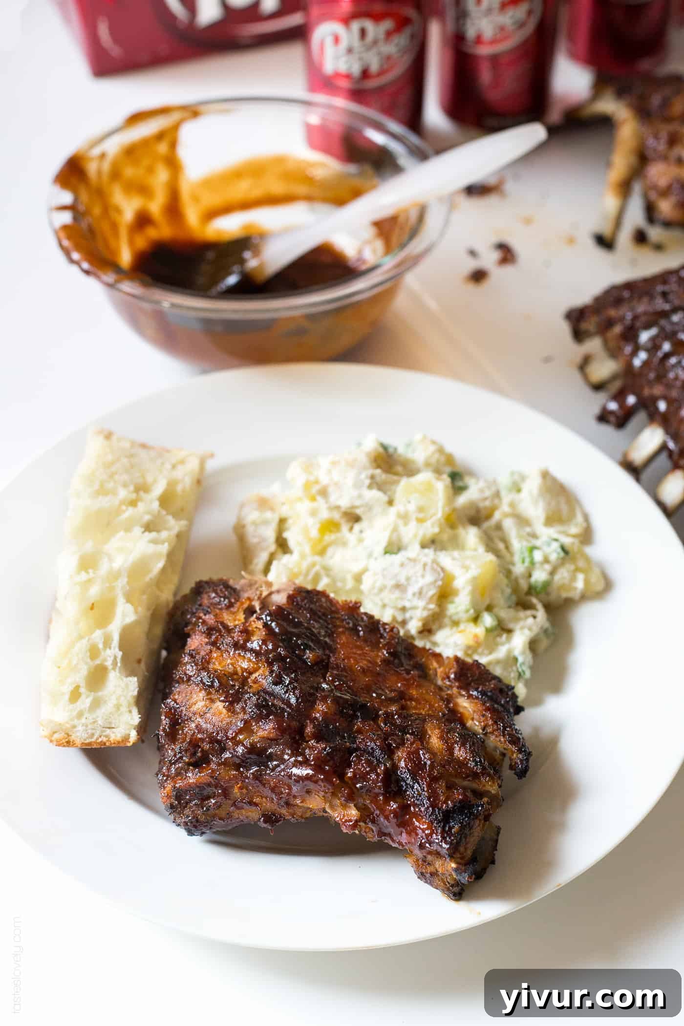 A plate of Dr Pepper ribs served with potato salad and bread, ready to enjoy.