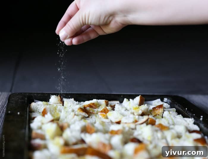 Crispy Garlic Parmesan Croutons 11 Garlic salt being sprinkled over the olive oil-drizzled bread cubes on a baking sheet.