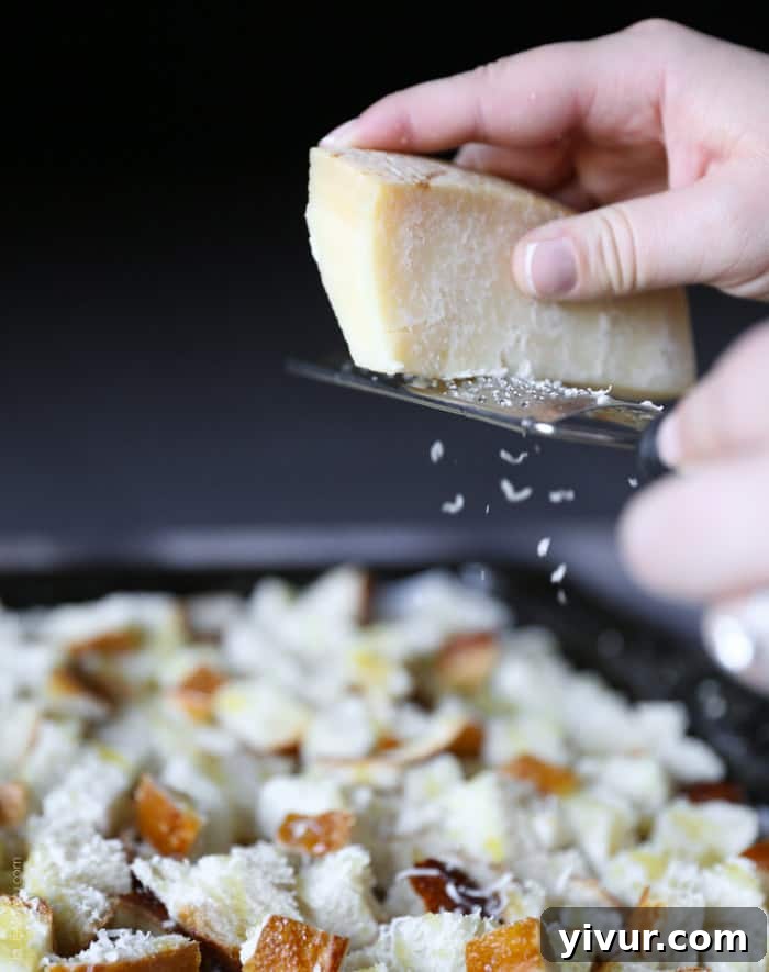 Crispy Garlic Parmesan Croutons 12 Freshly grated Parmesan cheese being sprinkled over the garlic-salted bread cubes on a baking sheet.