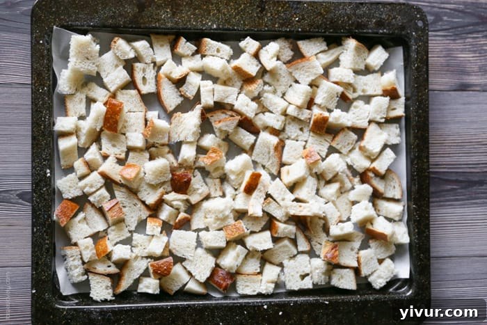 Crispy Garlic Parmesan Croutons 9 Cubed bread spread out in a single, even layer on a parchment-lined baking sheet, preparing for seasoning.