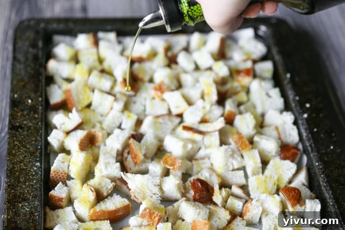 Crispy Garlic Parmesan Croutons 10 Olive oil being drizzled generously over the bread cubes spread on a baking sheet.