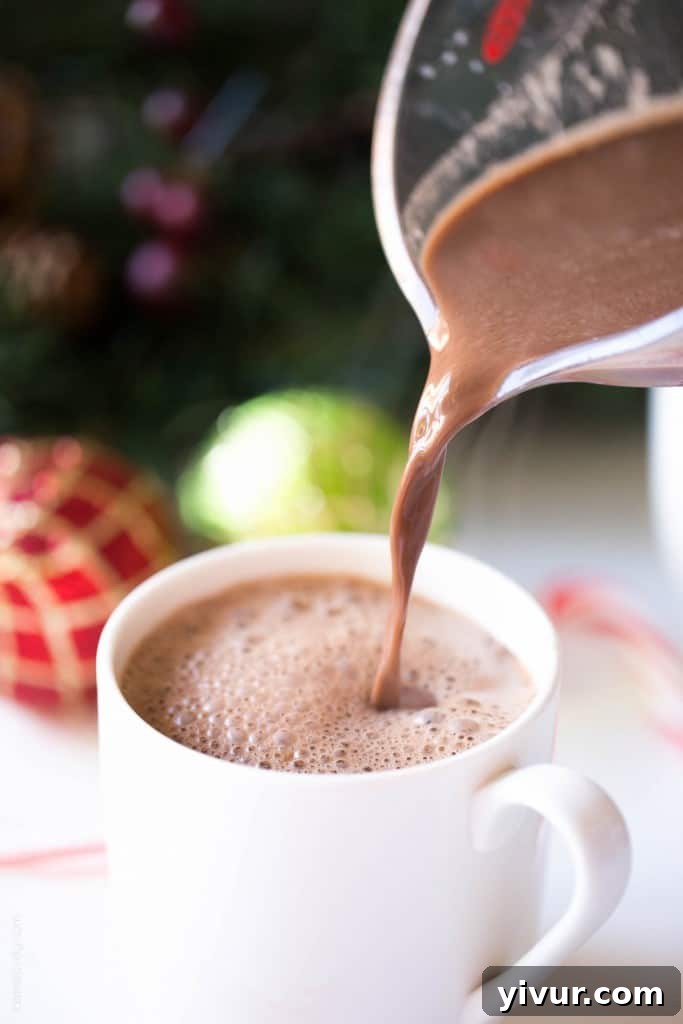 Close-up shot of a steaming mug of dairy-free hot chocolate, rich and dark, adorned with fluffy coconut whipped cream.
