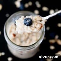 A closeup photo of a silver spoon holding blueberry overnight oats over a glass jar.
