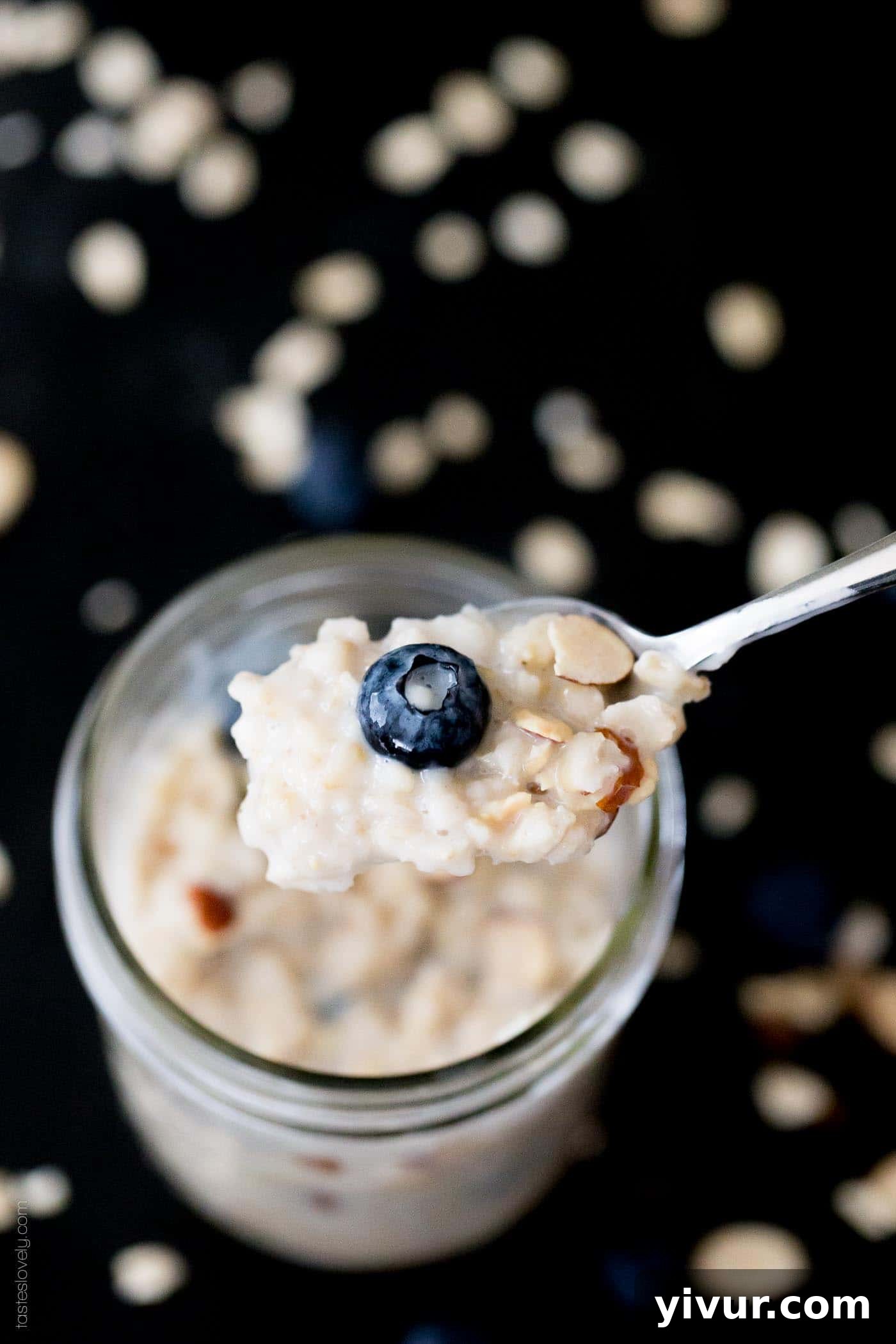 A closeup photo of a silver spoon holding blueberry overnight oats over a glass jar, showing the creamy texture and vibrant berries.