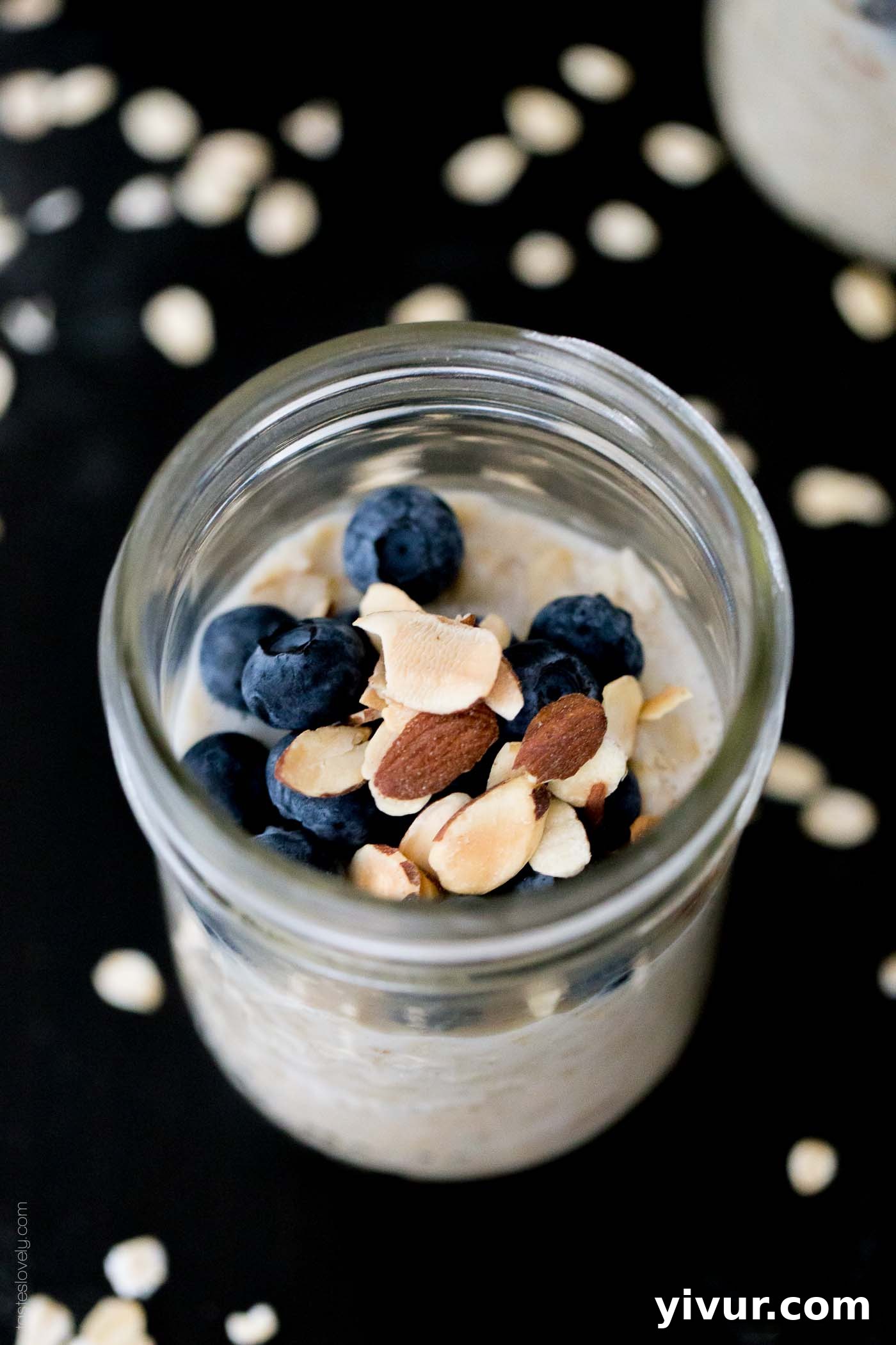 An overhead shot of overnight oats with protein powder in a glass jar and topped with blueberries and toasted almonds, invitingly presented.