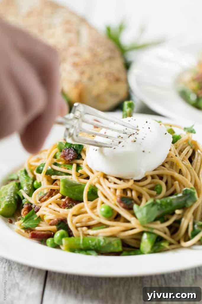 A bowl of freshly prepared Spring Pasta with Bacon and Poached Egg, topped with a runny egg yolk for extra creaminess.