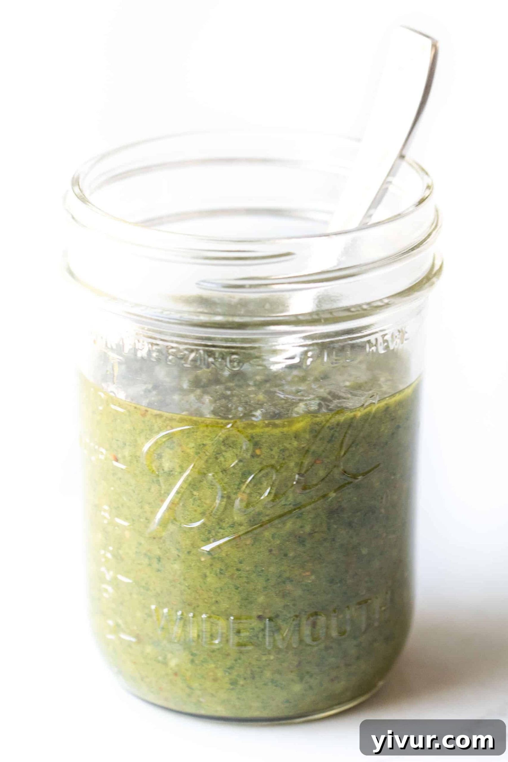 A mason jar filled with homemade dairy-free pesto, artfully arranged on a clean white surface for a minimalist presentation.
