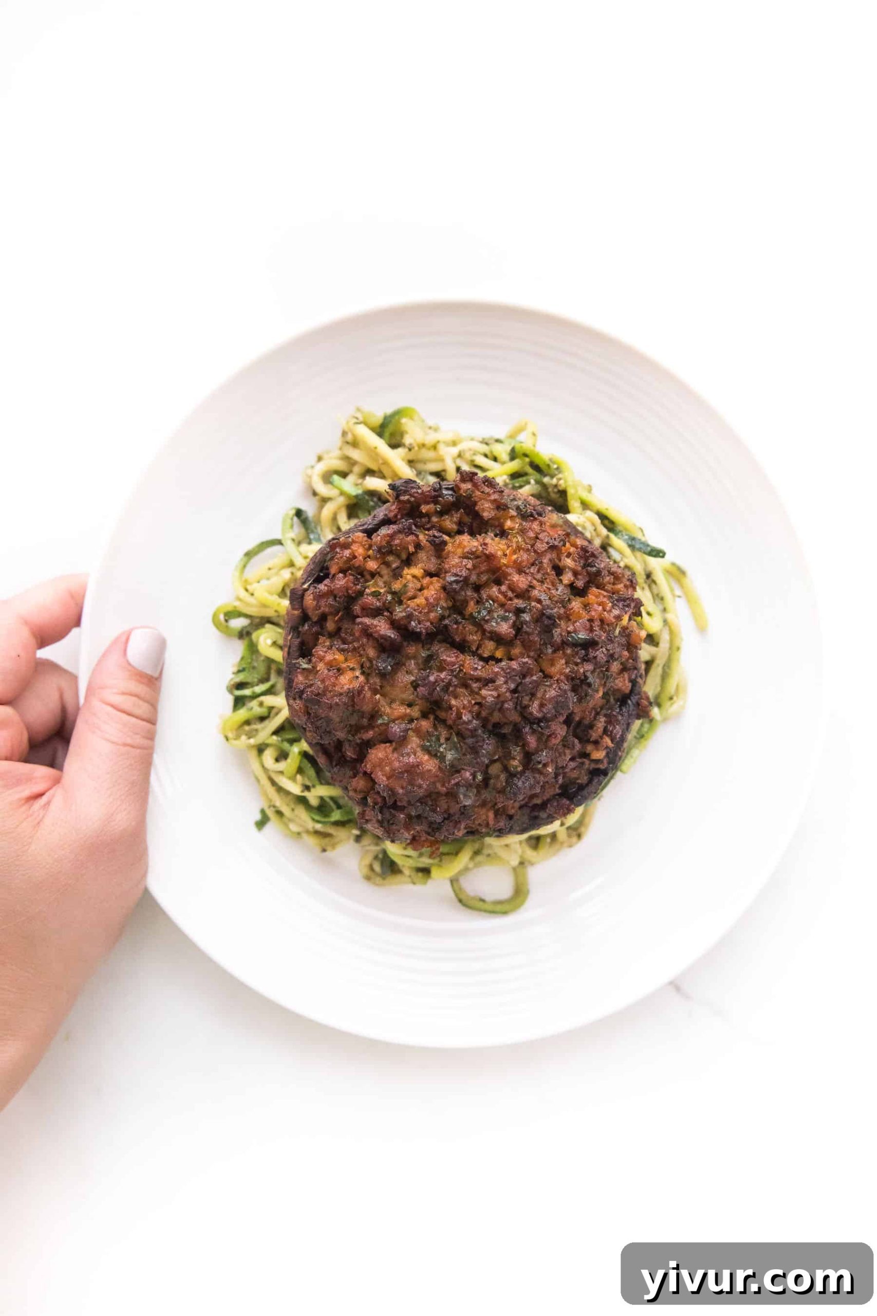 close up of sausage stuffed portobello mushrooms over zucchini noodles on a white plate