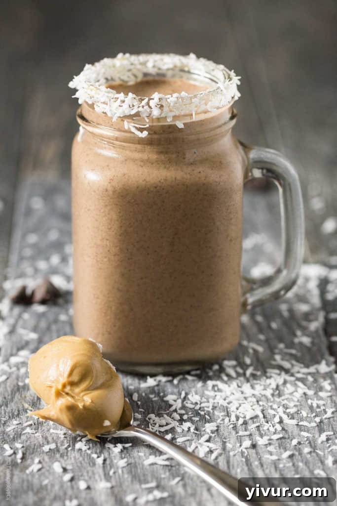 Creamy Peanut Butter Cocoa Coconut Smoothie in a tall glass, garnished with coconut flakes and chocolate shavings, set on a rustic wooden surface with fresh ingredients in the background.