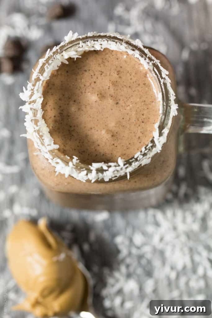 Ingredients for Peanut Butter Cocoa Coconut Smoothie laid out: a banana, a spoonful of peanut butter, cocoa powder, coconut flakes, and a cup of yogurt, all ready for blending.