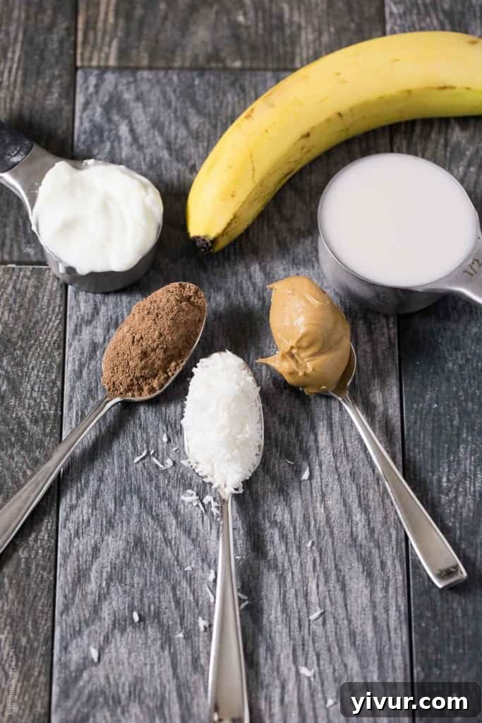 A glass of Peanut Butter Cocoa Coconut Smoothie on a kitchen counter, with a blender and various smoothie ingredients blurred in the background, highlighting a healthy morning routine.