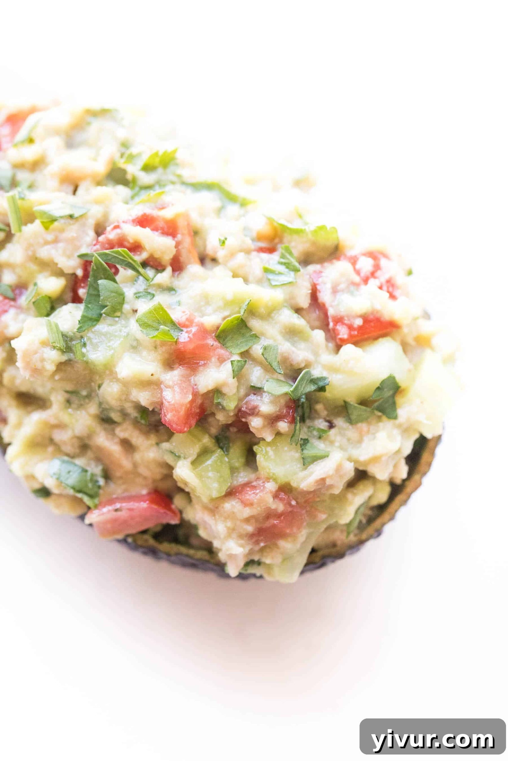 A close-up shot of avocado tuna salad elegantly served in an avocado boat, resting on a white surface