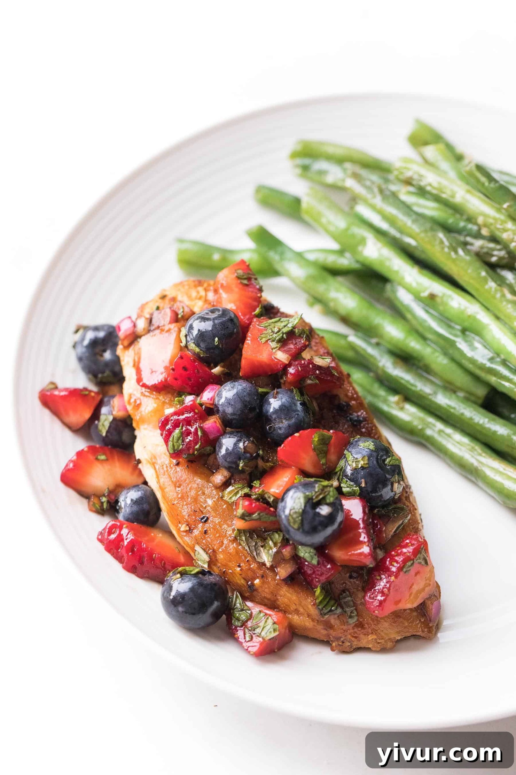 chicken topped with blueberry and strawberry salsa on a white plate and a white background