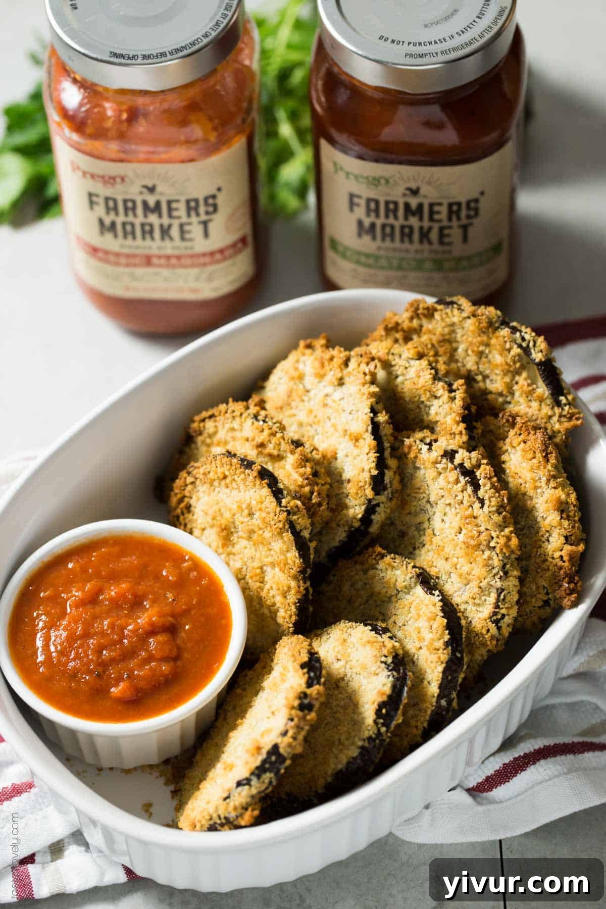 A hand dipping a crunchy baked eggplant bite into marinara sauce
