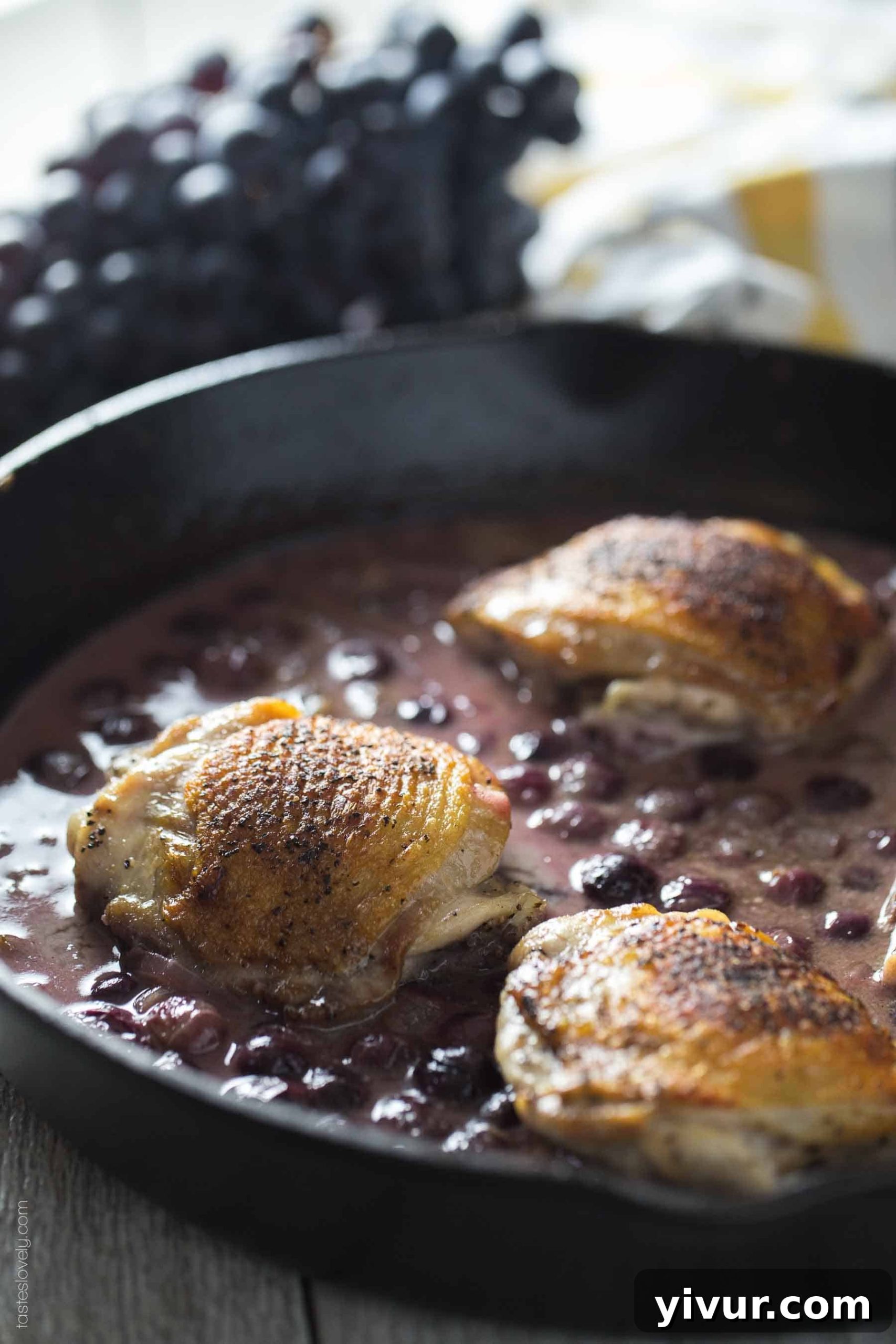 Crispy skin chicken thighs nestled in a pan with a rich mustard grape sauce, garnished with fresh herbs