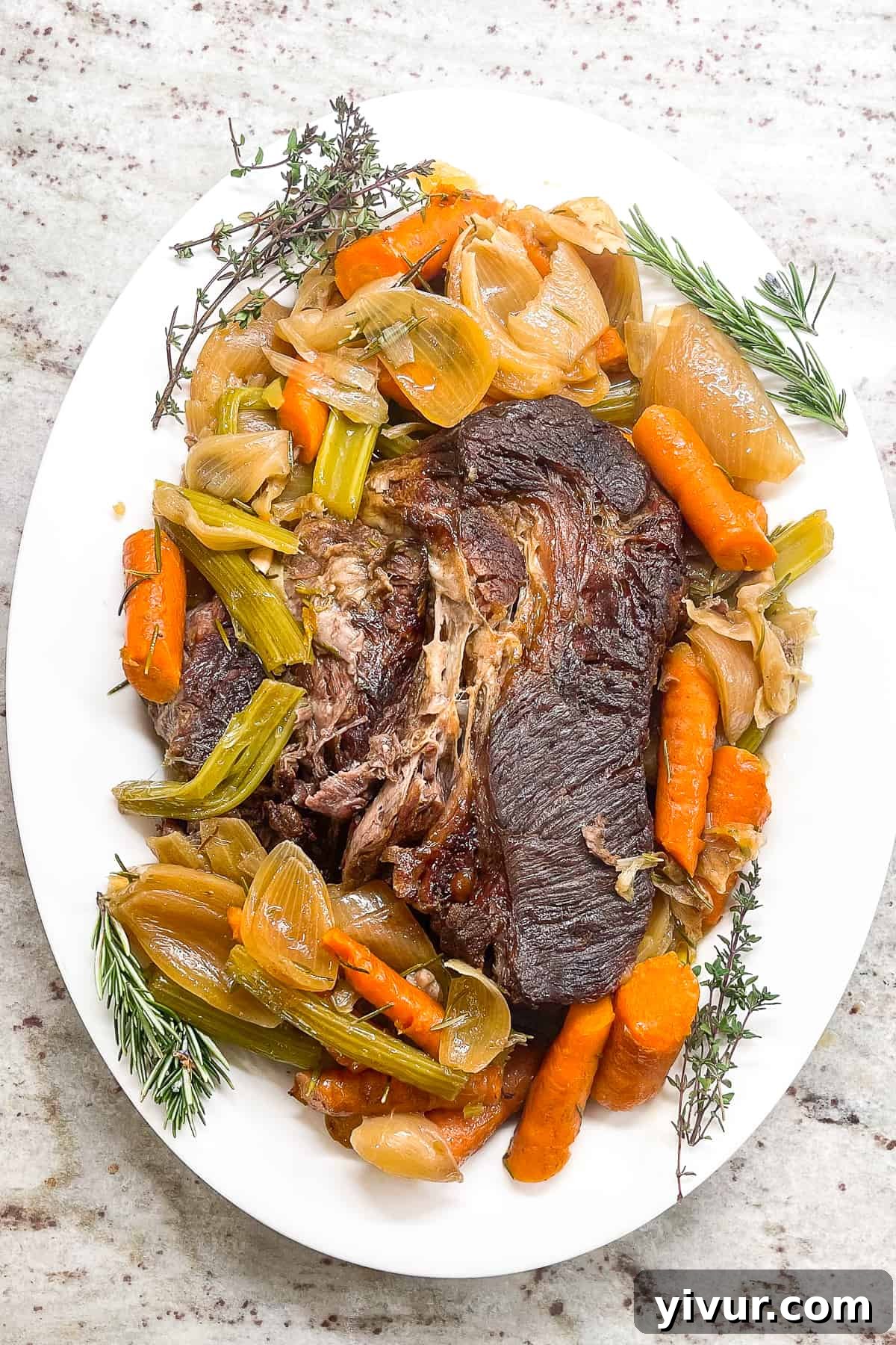 Fall-Apart Dutch Oven Pot Roast Smothered in Rich Gravy 3 A beautiful Dutch oven pot roast served on a white platter, adorned with perfectly cooked onions, carrots, and celery, ready to be enjoyed.