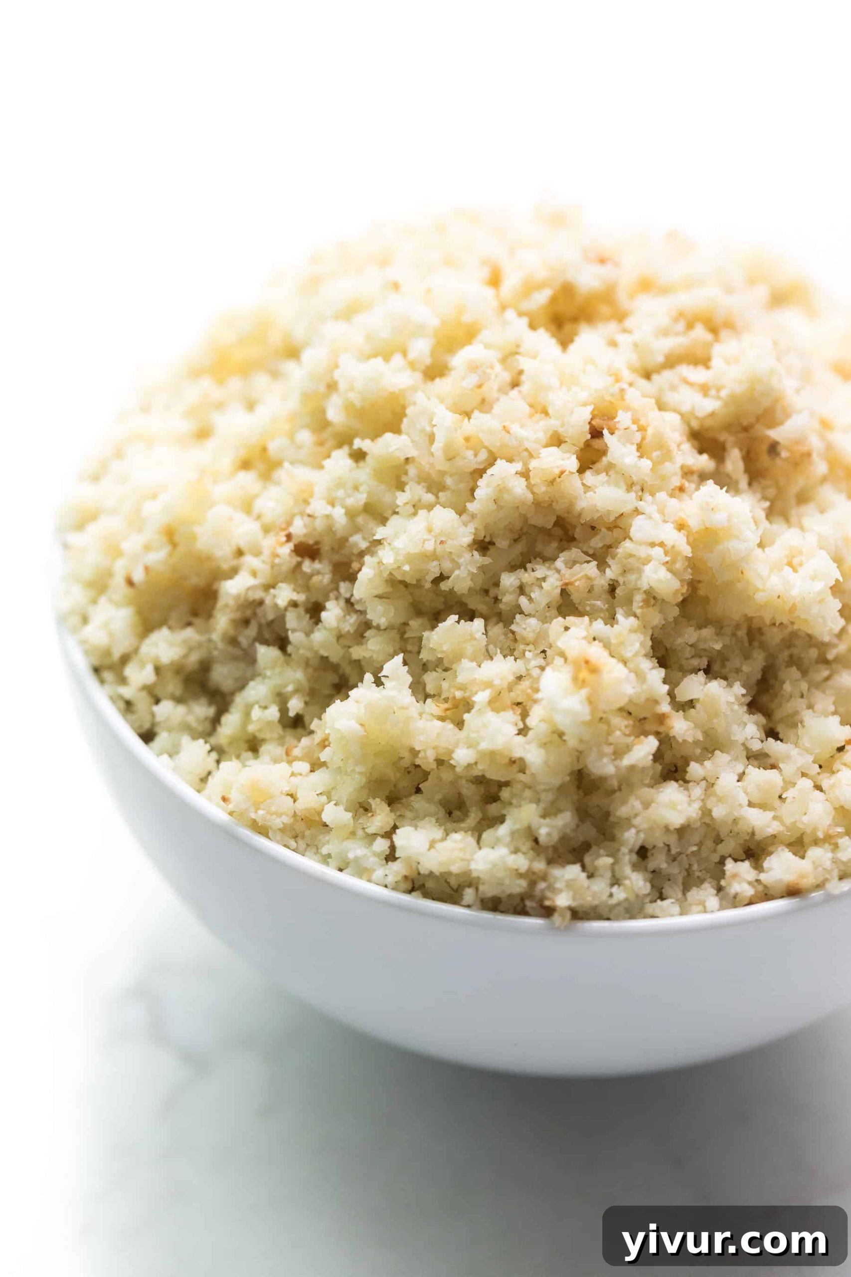 A close-up view of fluffy, perfectly textured homemade cauliflower rice in a white bowl, highlighted by natural light.