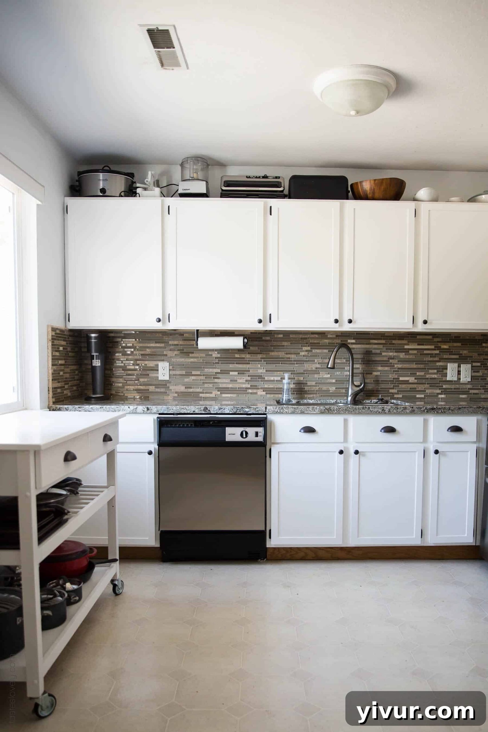 Finished kitchen remodel with white shaker cabinets, stainless steel dishwasher, and white island cart