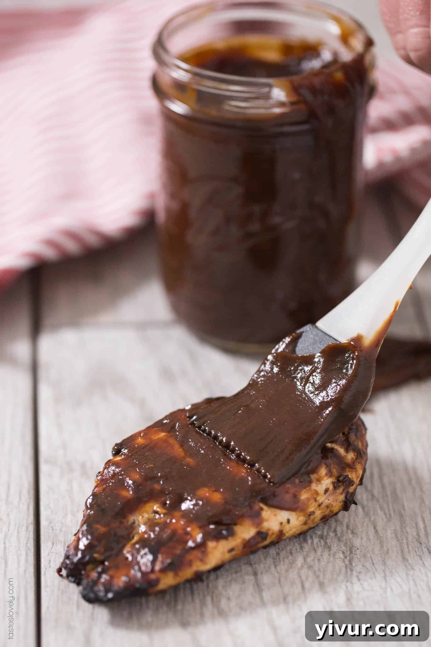 Brushing keto BBQ sauce on grilled chicken breast with char marks.