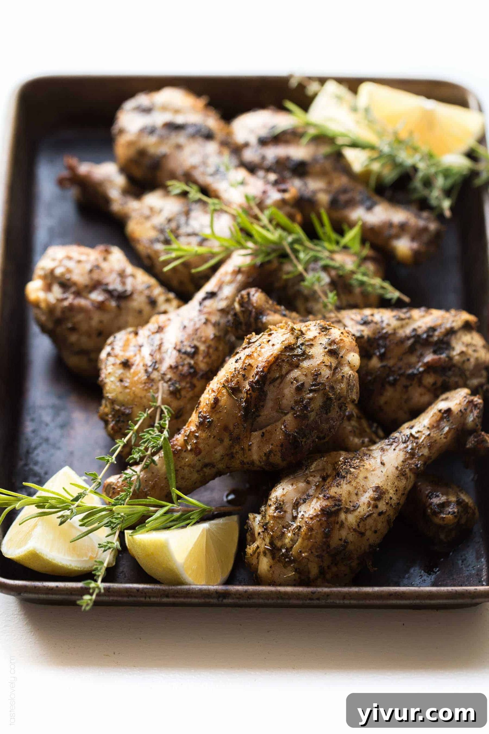 Two perfectly grilled lemon herb chicken drumsticks on a rustic wooden board, garnished with fresh lemon slices and rosemary sprigs, highlighting the crispy skin.