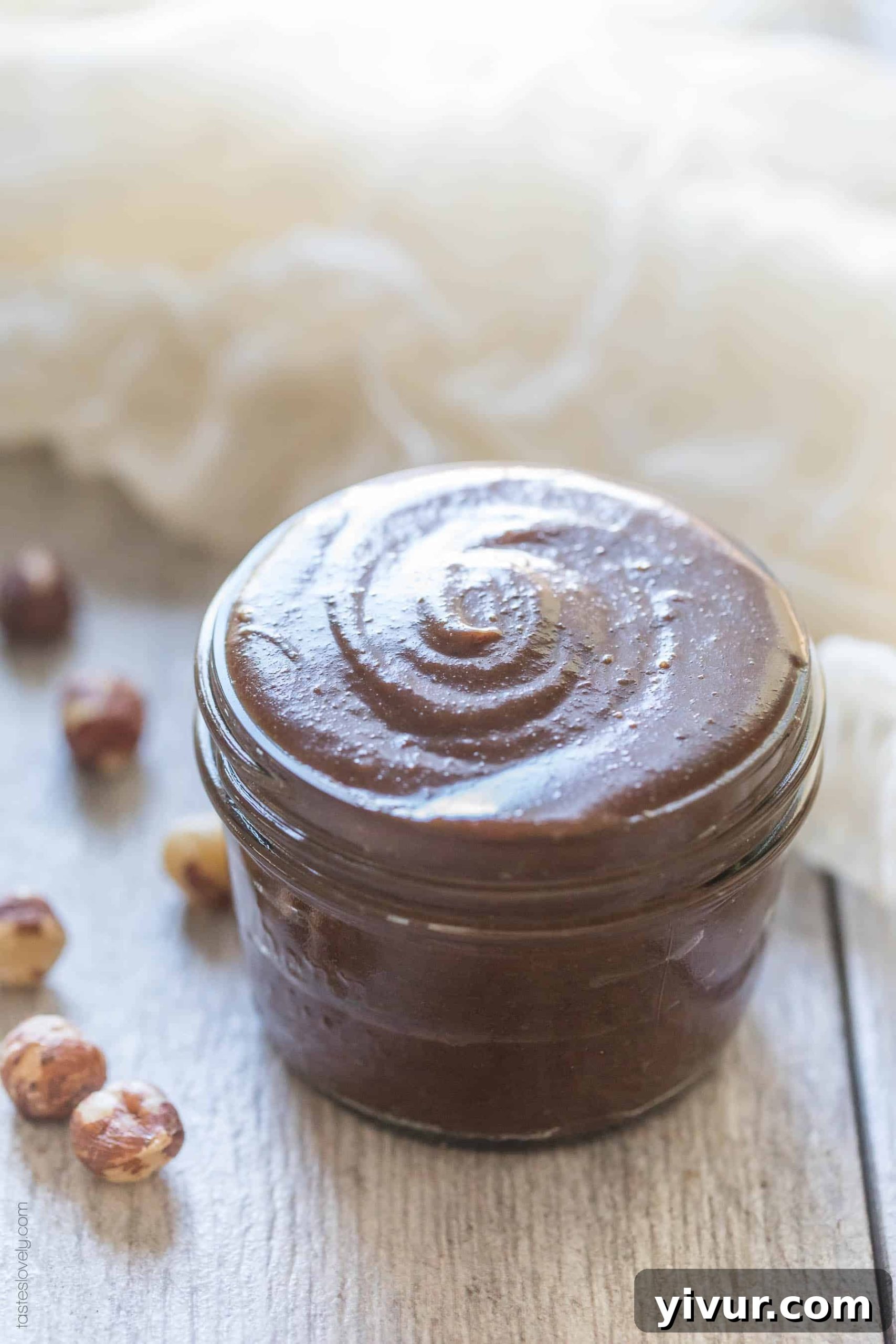 A jar of homemade Paleo Nutella being spread on a piece of fruit, highlighting its creamy texture.