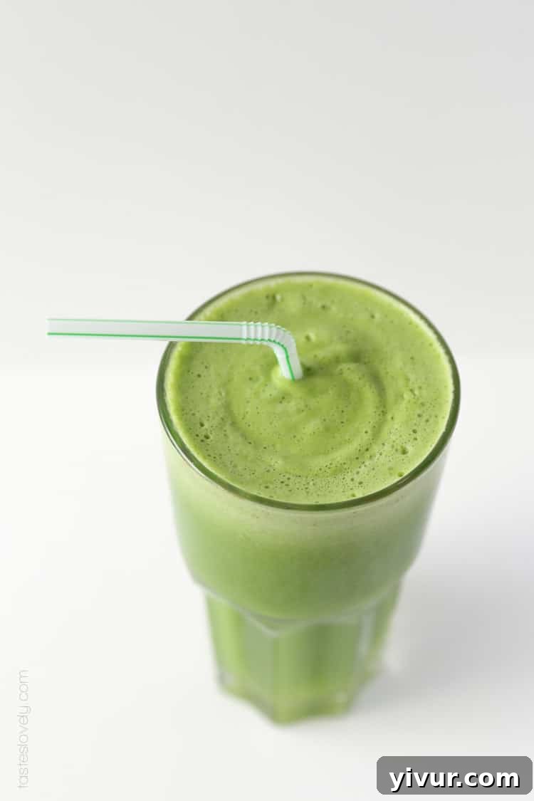 An overhead shot showcasing a glass of radiant green smoothie, complete with a plastic straw, on a light background.