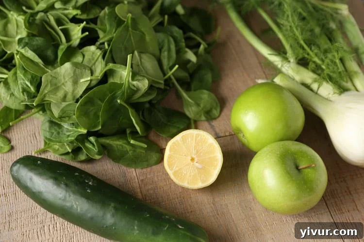 A selection of fresh ingredients including spinach, half a lemon, crisp cucumber, vibrant green apples, and a robust fennel bulb, artfully arranged.