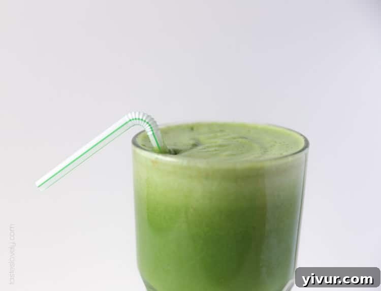 A tall glass filled with freshly juiced detox green juice, complete with a straw, reflecting its vibrant color.