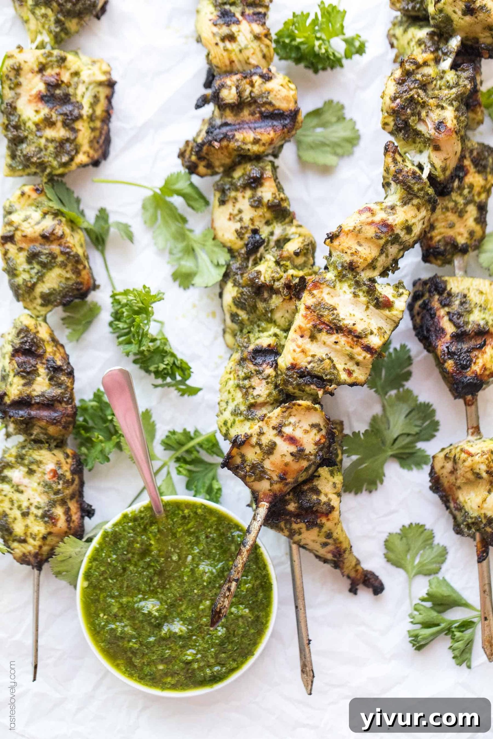 Two grilled Paleo + Whole30 Chimichurri Chicken Skewers on a plate, with a small bowl of extra chimichurri sauce for dipping. This healthy and quick chicken kebab is great for families.