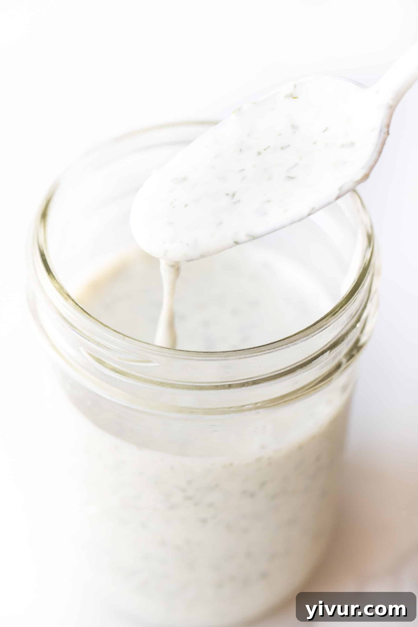 A spoon dripping homemade Whole30 and Keto ranch dressing into a mason jar.