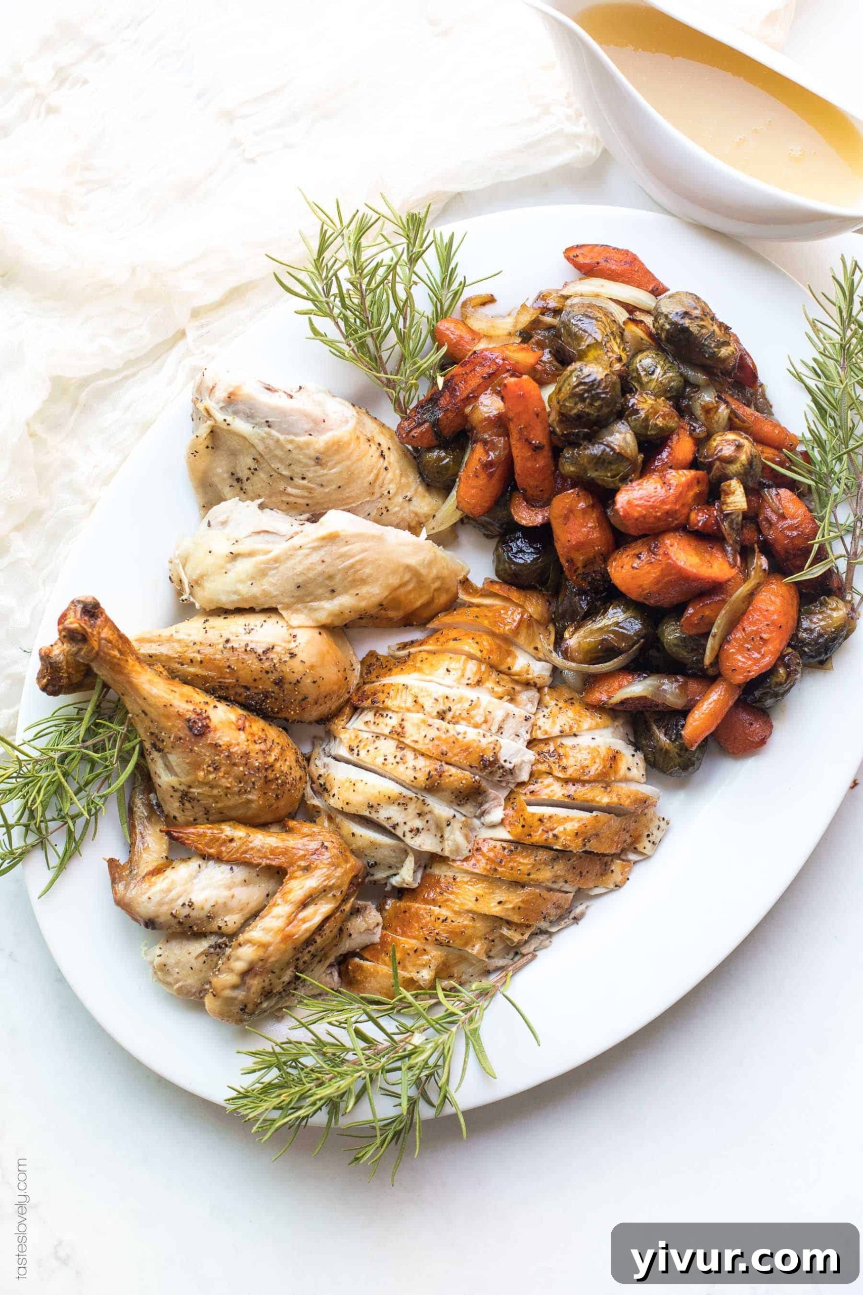 Cut up roast chicken on a platter with roasted root vegetables and sprigs of rosemary herbs
