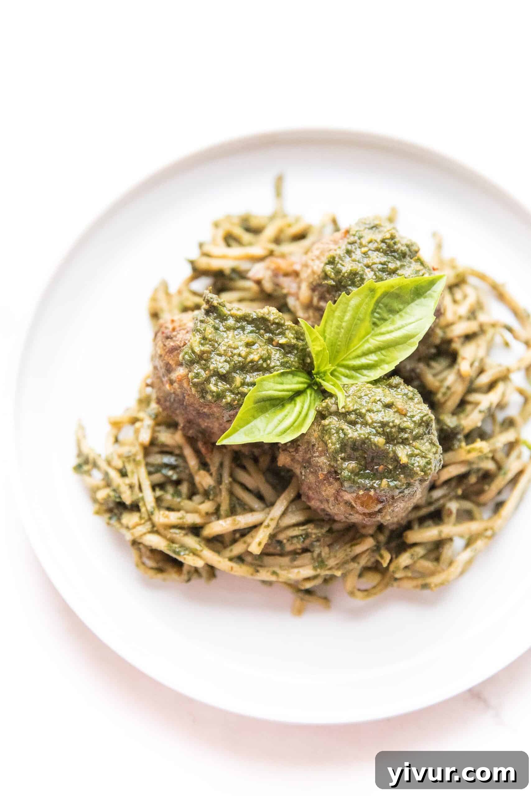 Pesto meatballs served on a bed of pesto-coated hearts of palm noodles, garnished with fresh basil leaves.