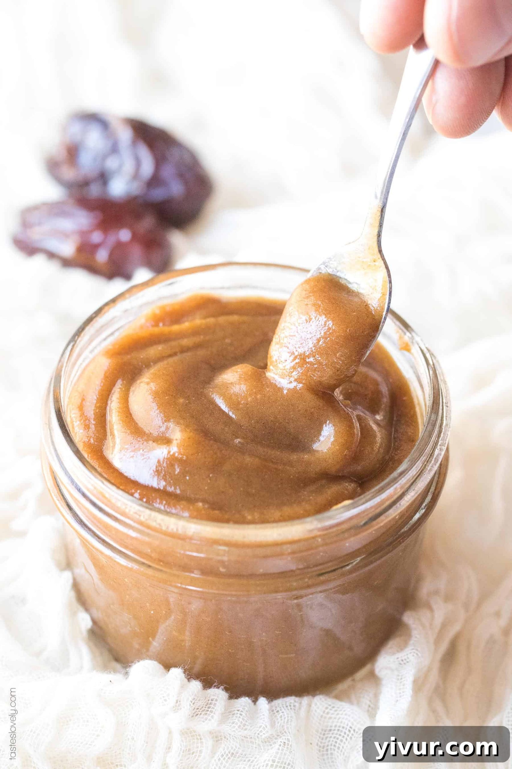 A spoon resting inside a jar of freshly made date paste, showcasing its rich, caramel-like texture.