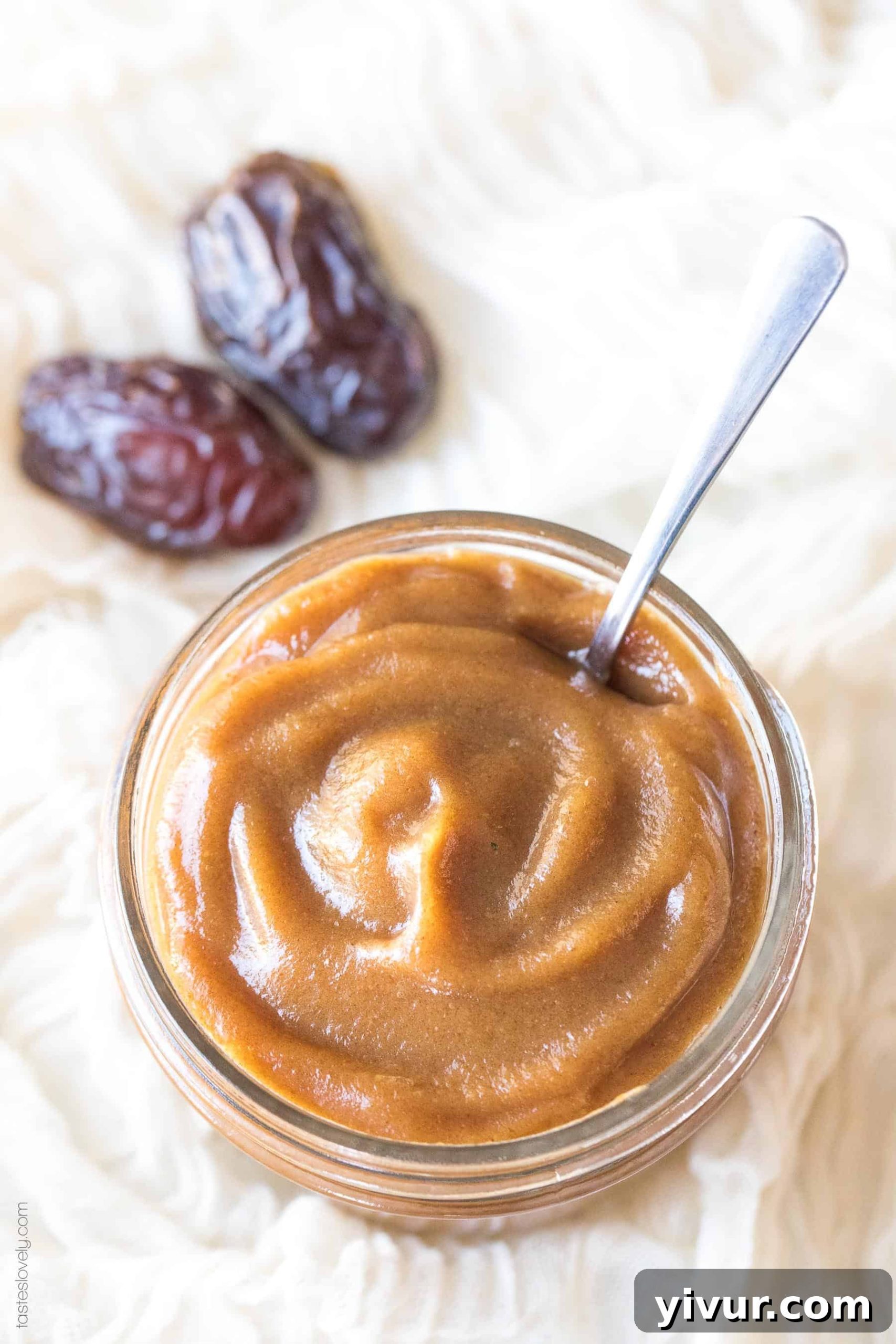 A jar of smooth date paste with a spoon, accompanied by two plump Medjool dates, highlighting the source of this natural sweetener.