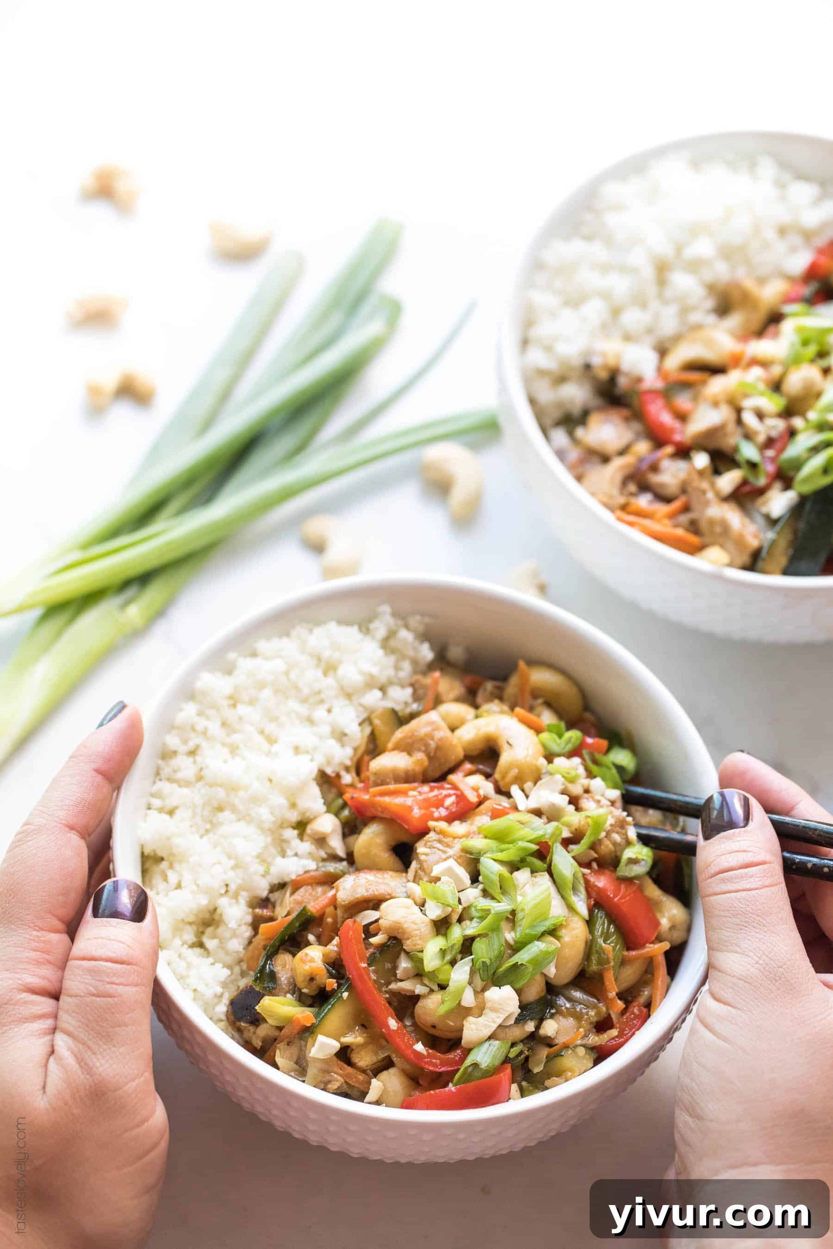2 hands holding a bowl with chicken stir fry and cauliflower rice and chopsticks