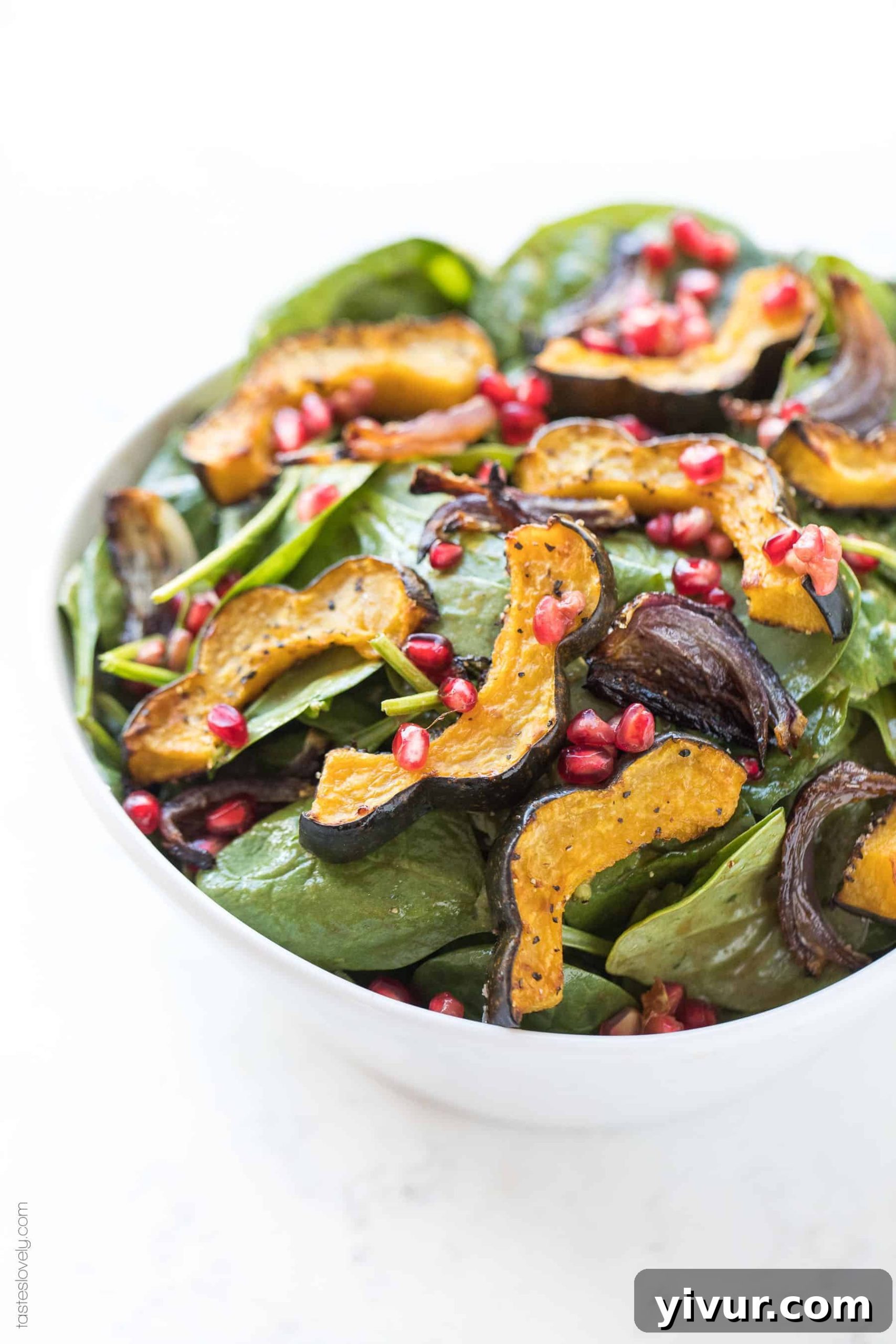 Vibrant spinach salad with golden roasted acorn squash chunks, caramelized onions, and ruby red pomegranate seeds, dressed in a balsamic vinaigrette.