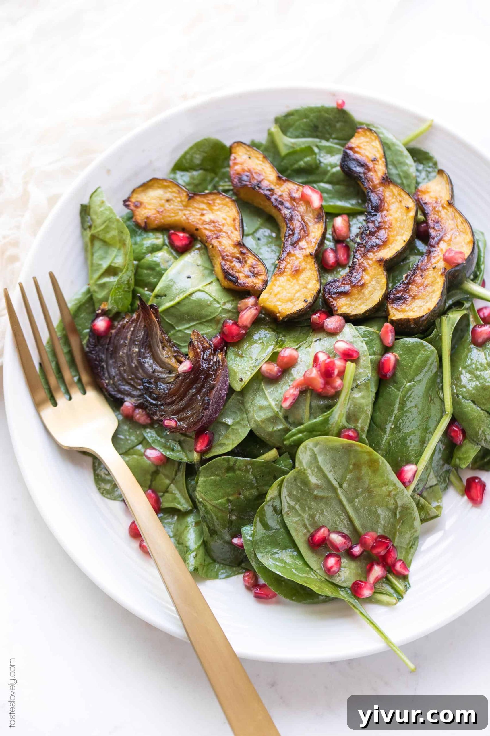 Close-up of a bowl of fresh spinach salad featuring roasted acorn squash, roasted red onions, and glistening pomegranate arils, ready to be tossed.