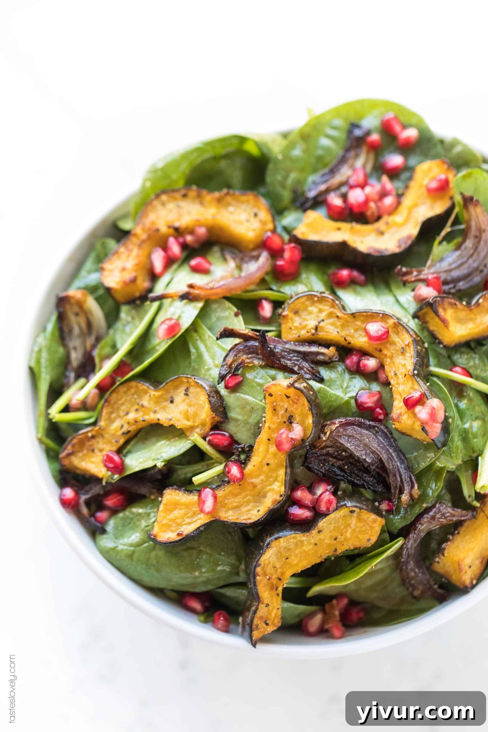 A beautifully composed bowl of Roasted Acorn Squash Spinach Salad, glistening with balsamic vinaigrette and topped with a generous sprinkle of pomegranate seeds.