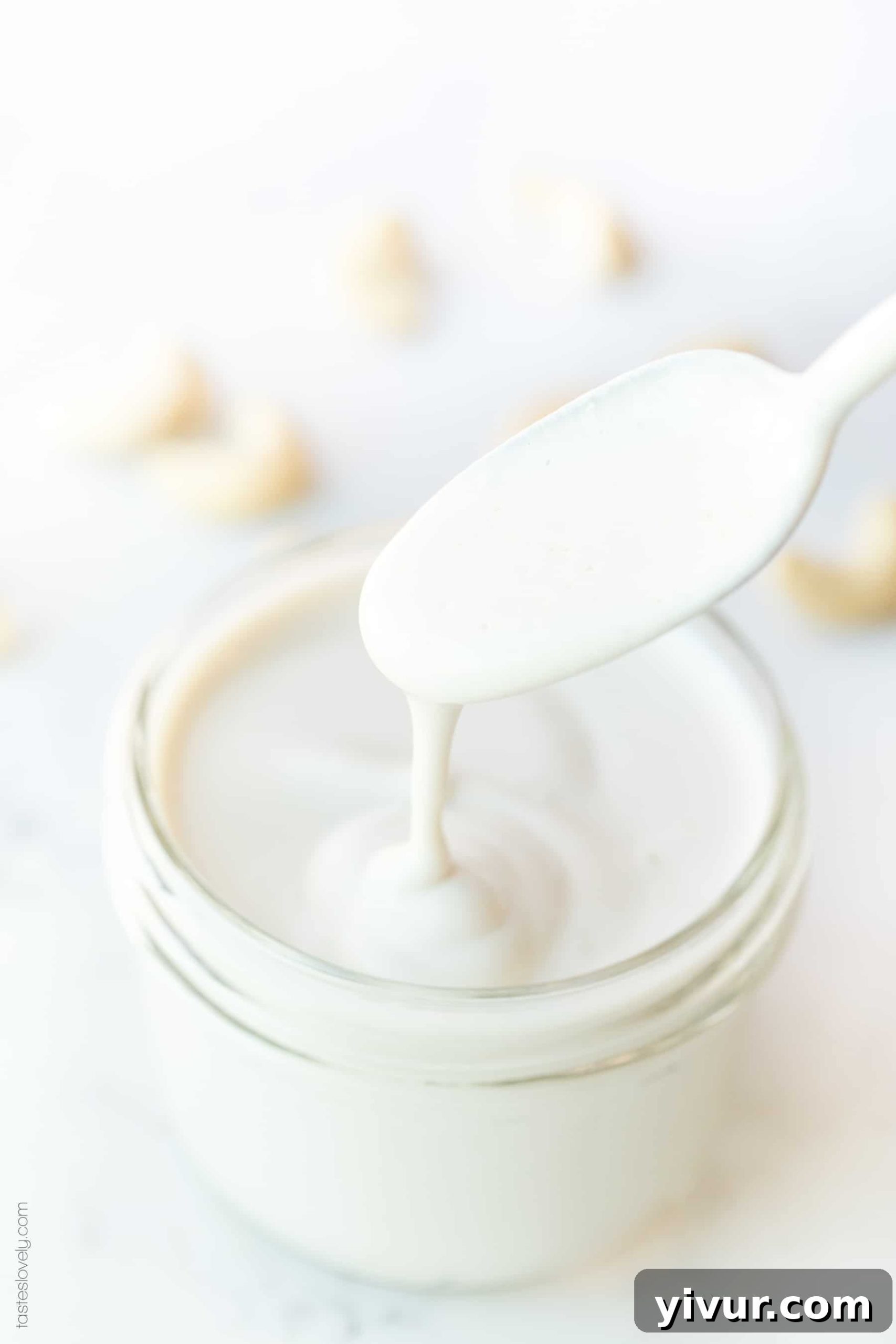 A spoon drizzling cashew cream into a glass jar, highlighting its smooth texture.