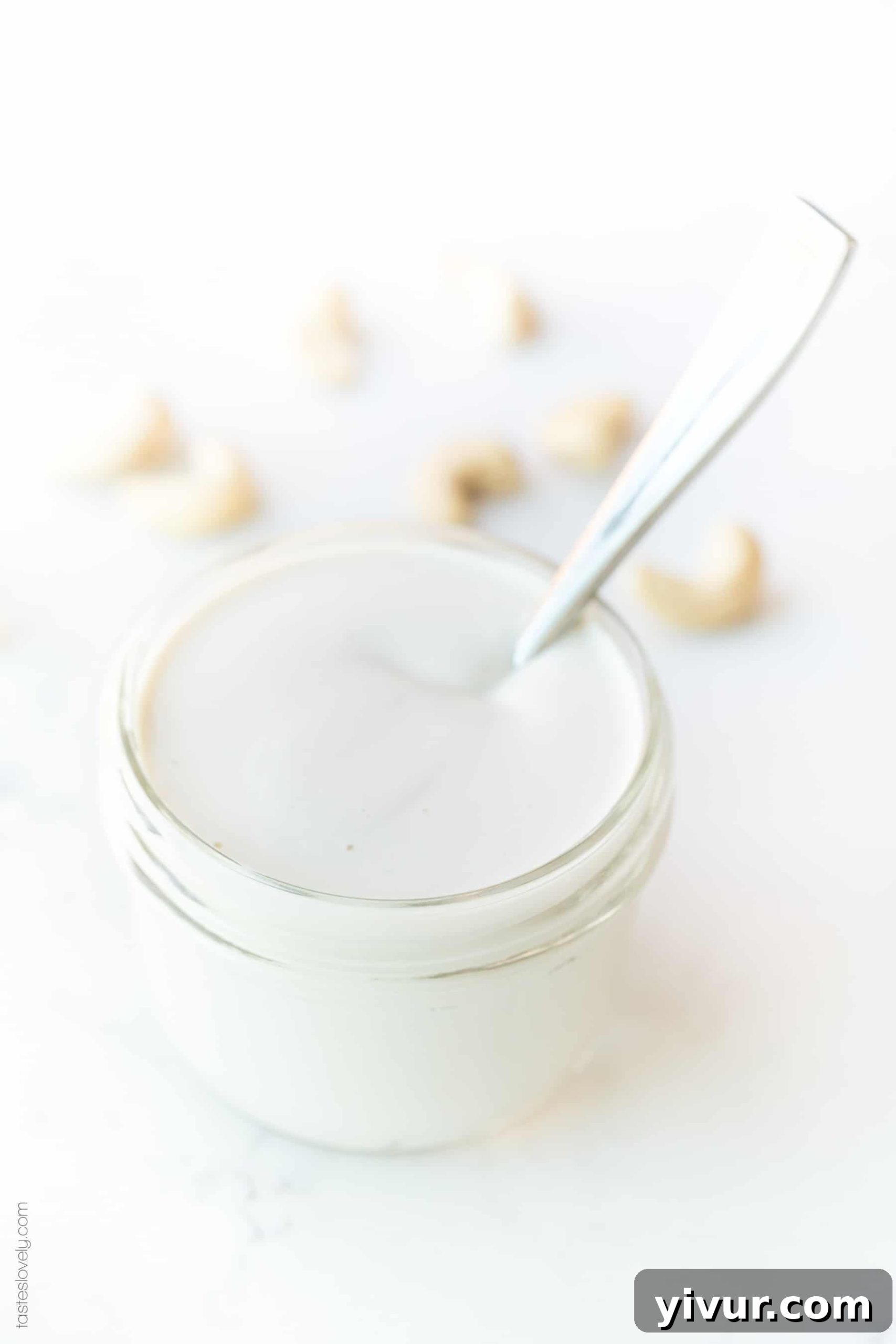 A glass jar filled with creamy cashew cream, with a small spoon resting on the rim.