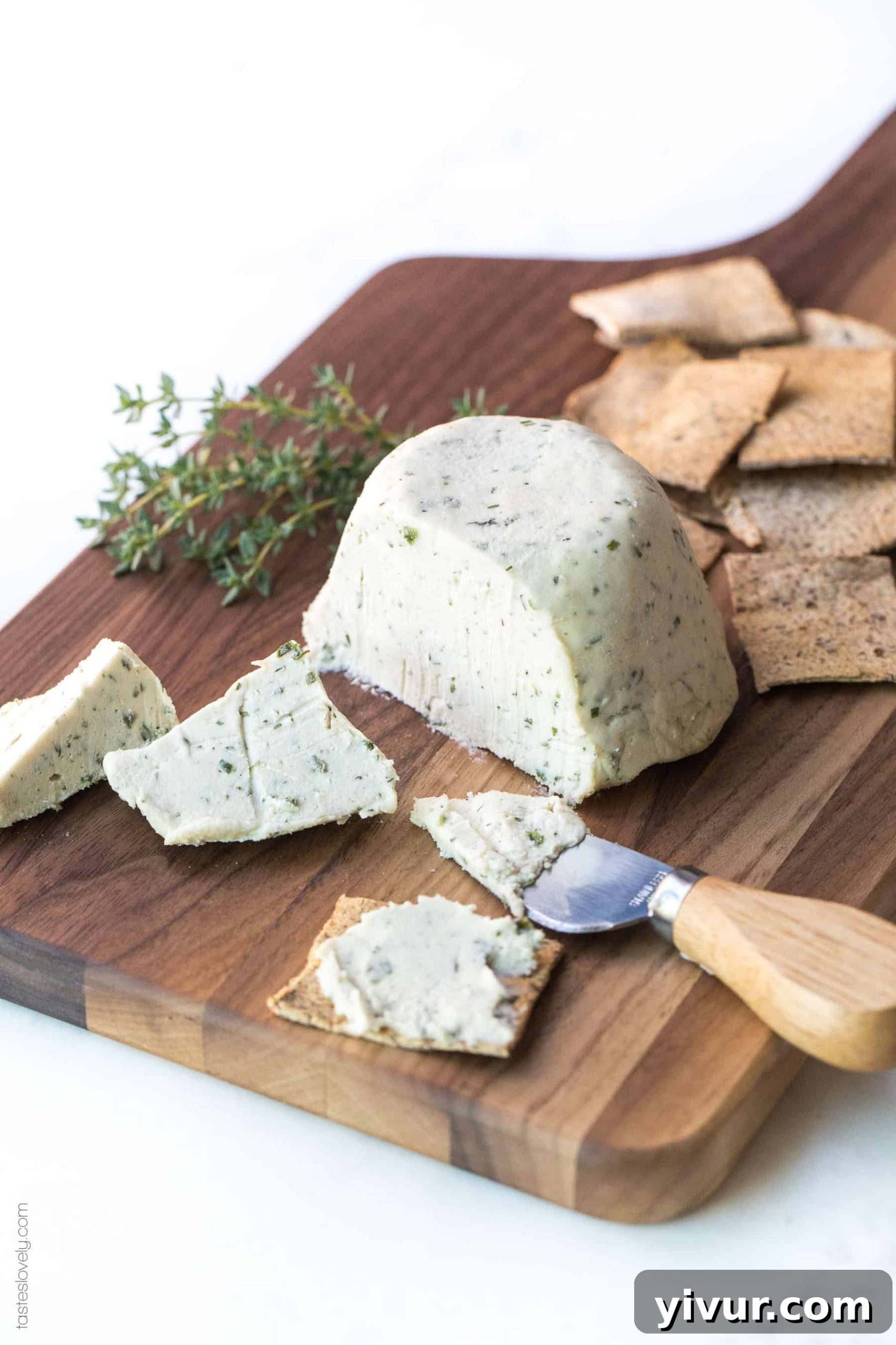 Herbed Cashew Cheese sliced on a wooden board, surrounded by artisan crackers and fresh herbs, perfect for a healthy, dairy-free appetizer.