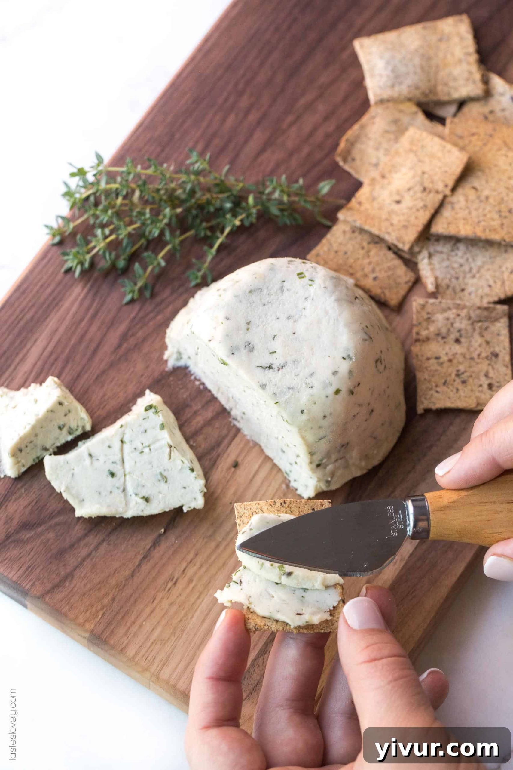 Close-up of creamy Herbed Cashew Cheese on a rustic wooden board, garnished with fresh rosemary and served with gluten-free crackers, showcasing its rich texture.