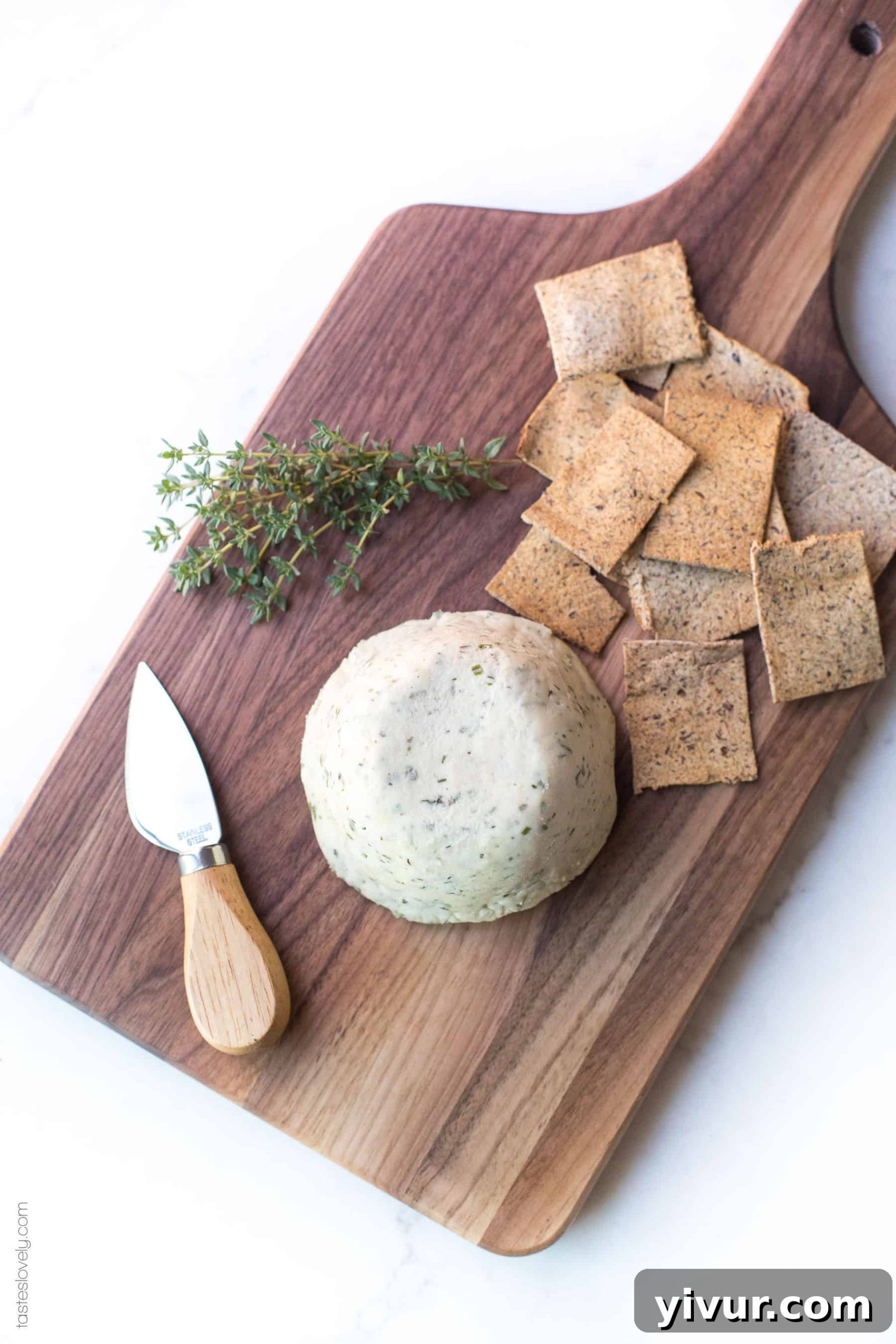 Herbed Cashew Cheese elegantly sliced and served on a wooden board, accompanied by various healthy crackers and fresh garnishes, ready to be enjoyed.